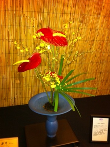 Red Anthuriums, yellow Oncidium Orchids and Papyrus are combined in an Ikenobo arrangement.